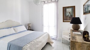 A bedroom with a bed, a nightstand, a lamp, a painting, and a wooden cabinet. - Apartment Near the Sea and the Center of San Vito lo Capo (San Vito Lo Capo)