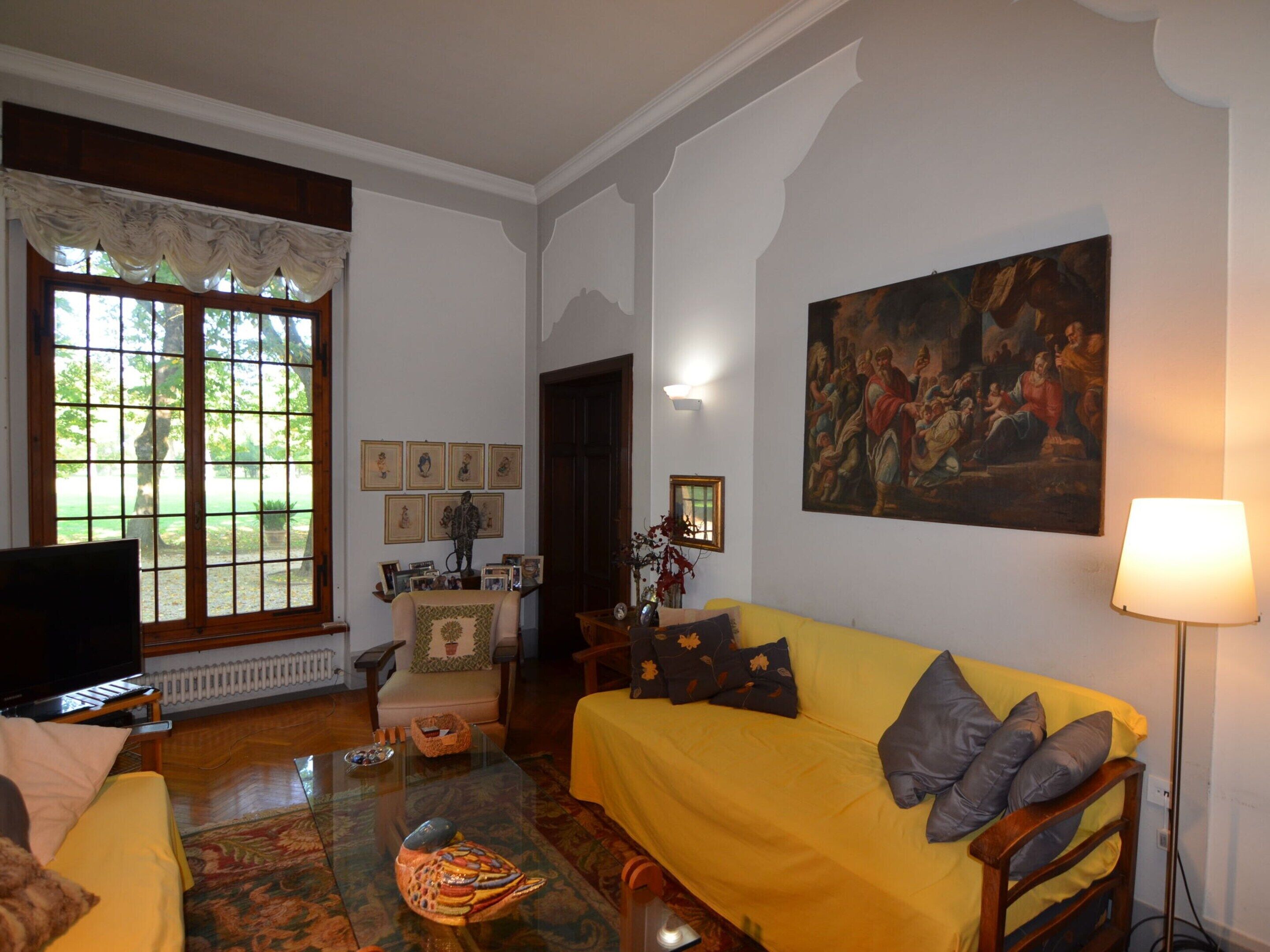 Una sala de estar con un sofá amarillo, una mesa de centro de vidrio, un televisor y un cuadro en la pared.