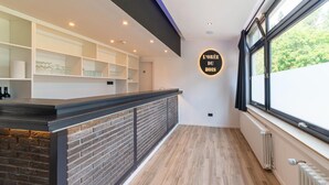 A modern hotel lobby with a brick accent wall, a reception desk, and a large window offering a view of greenery. - Mansion With Pool & Bar (Buellingen)