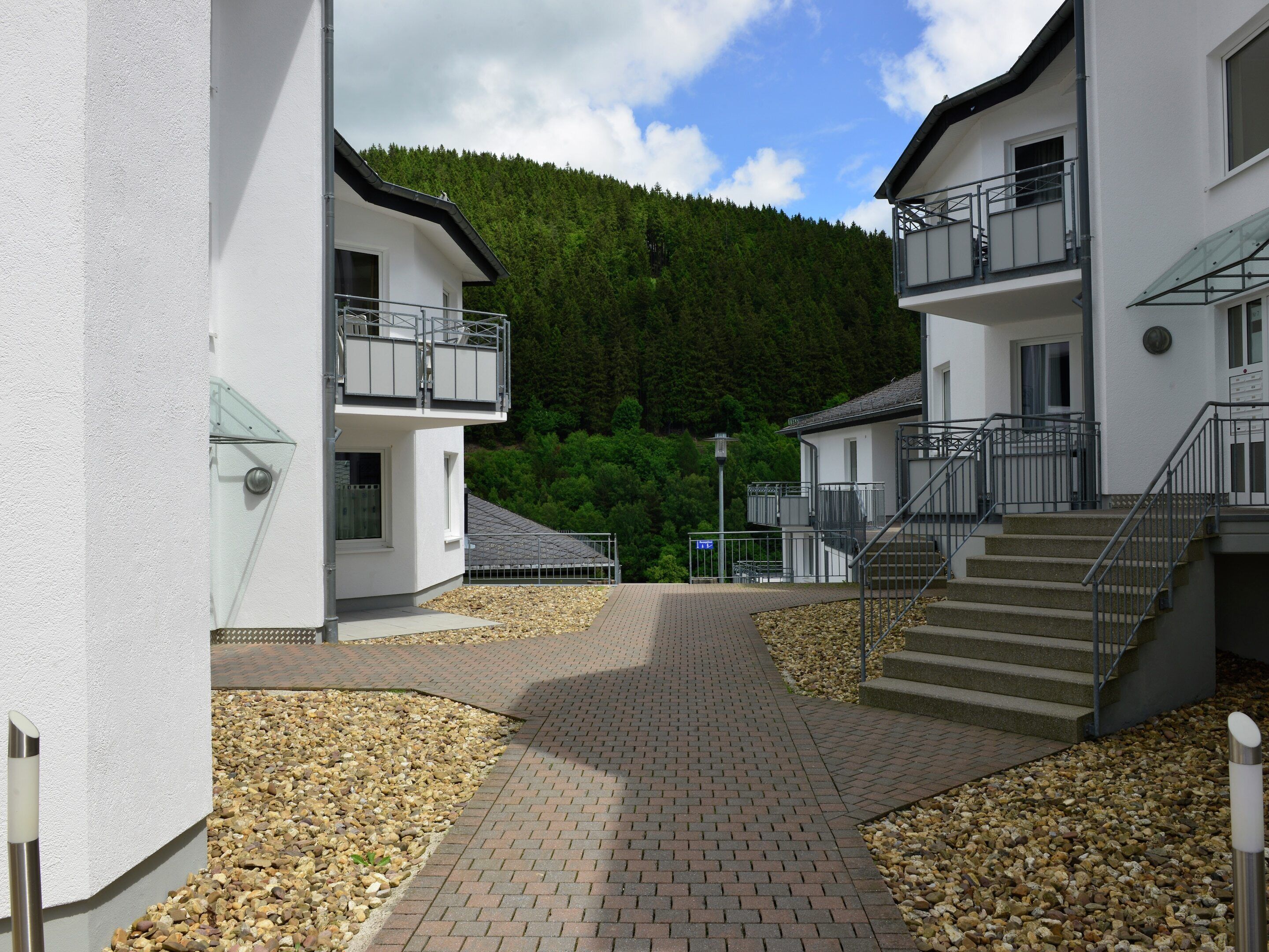 A modern building with a paved walkway, a staircase, and a view of a forested hill.