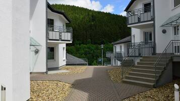 A modern building with a paved walkway, a staircase, and a view of a forested hill.
