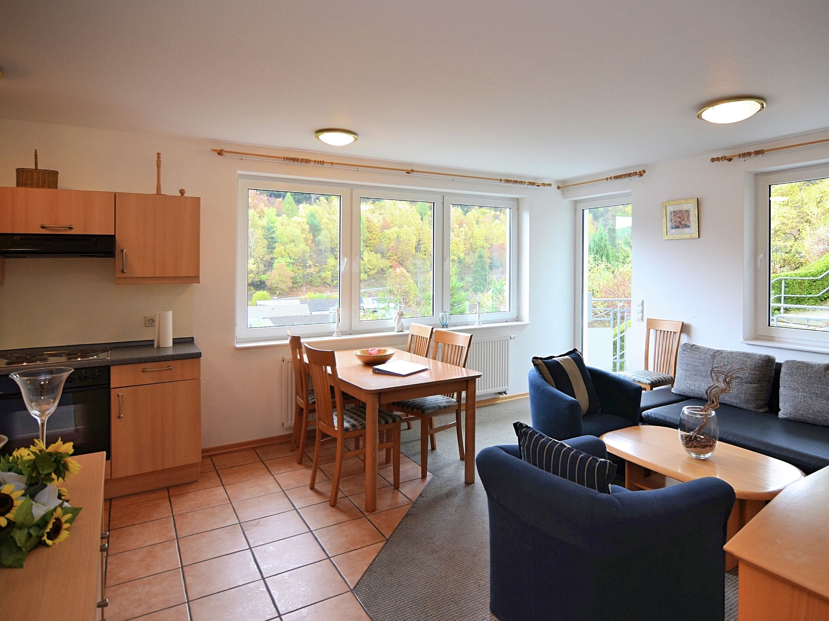 A kitchen with a dining table and chairs, a sofa, and a window with a view of trees.