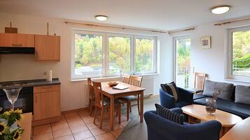 A kitchen with a dining table and chairs, a sofa, and a window with a view of trees.
