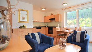 A modern kitchen with wooden cabinets, a dining area with blue sofas, and a large window with a forest view. - Wohnung in der Nahe der Hessischen Berge (Willingen)