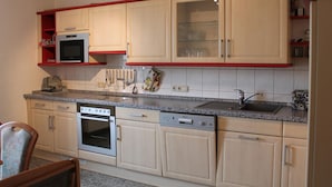 Une cuisine avec des meubles de couleur beige, un four à micro-ondes, un four traditionnel, un lave-vaisselle et un plan de travail en granit.