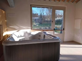 A modern bathroom with a freestanding bathtub, a large window with a view of a garden, and a wooden ceiling.