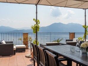 An outdoor patio with wicker furniture, a table, and a view of mountains and a lake. - Belvilla by OYO Panoramica (Oggebbio)