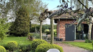 Un giardino con un vialetto lastricato, una sedia di plastica bianca e un edificio in mattoni con una porta scura.