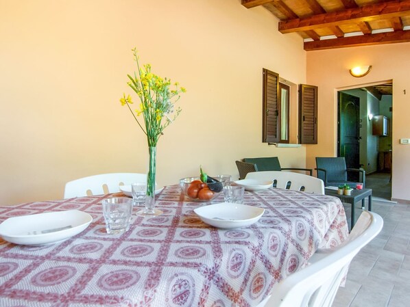 Un coin repas avec une table dressée pour deux personnes, un vase rempli de fleurs jaunes et une vue sur la cuisine par une porte ouverte.