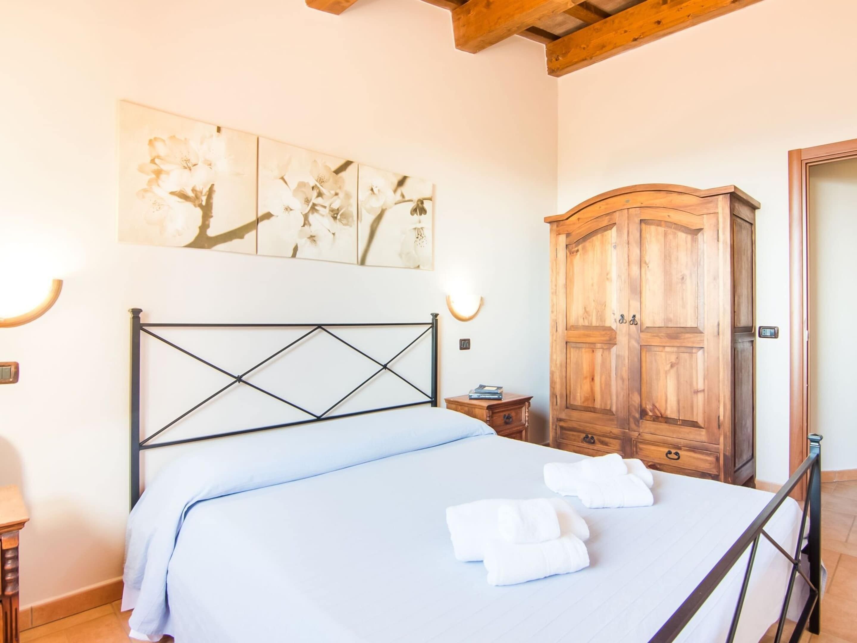 A bedroom with a bed, a wooden wardrobe, and a wall-mounted light fixture.