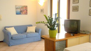 A living room with a blue sofa, a small table with a television, and a potted plant. - Residence and Quiet Residence With Pool, Near the Lake (Lazise)