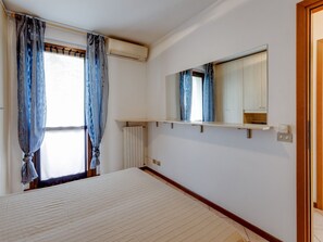 A bedroom with a large bed, a window with curtains, an air conditioning unit, a mirror, and a shelf with a radio. - Residence and Quiet Residence With Pool, Near the Lake (Lazise)
