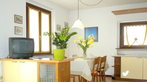 A compact kitchen with a dining area, a television on a cabinet, and a potted plant. - Residence and Quiet Residence With Pool, Near the Lake (Lazise)