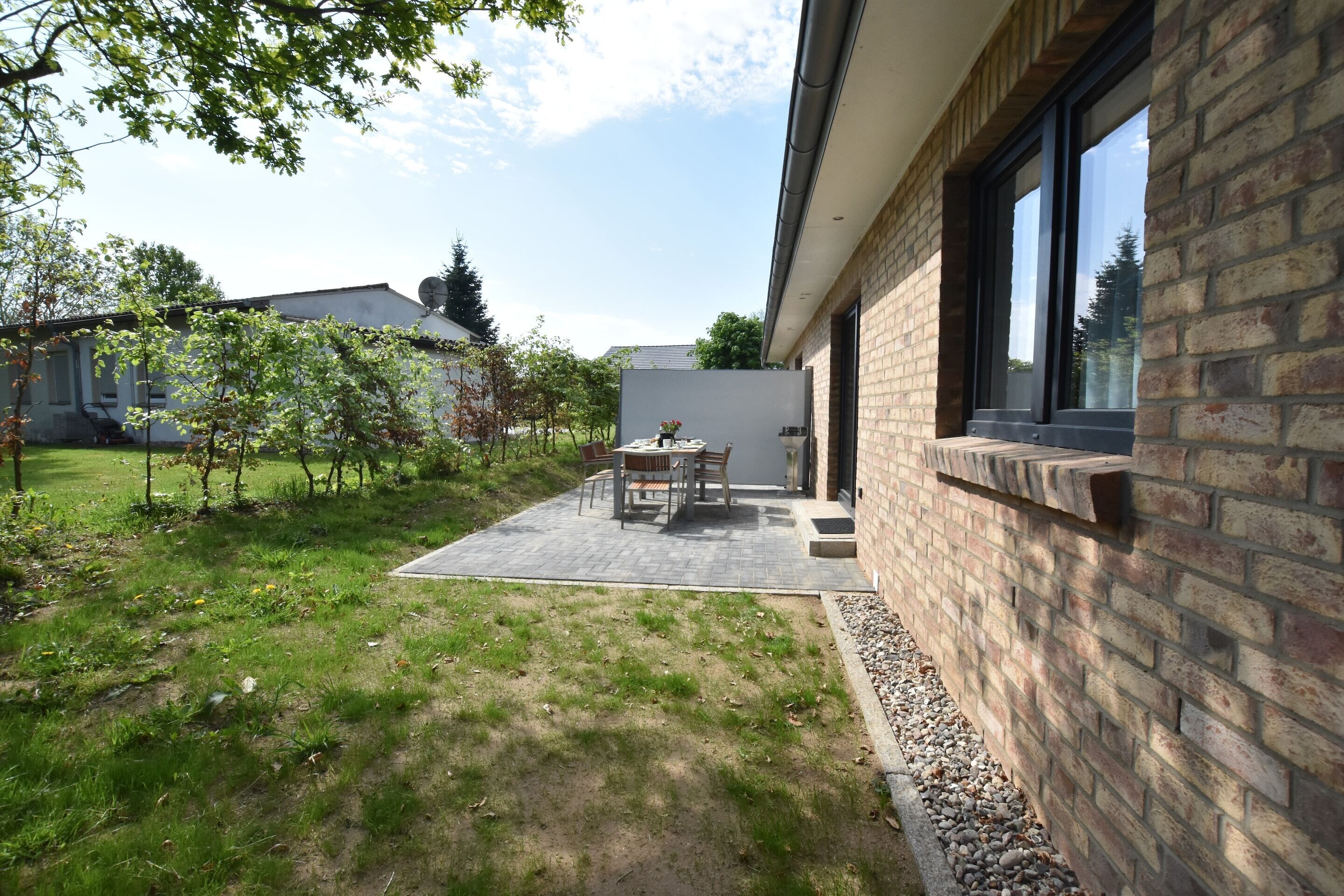 Un’area patio con tavolo e sedie, un muro in mattoni e vista su una proprietà vicina.