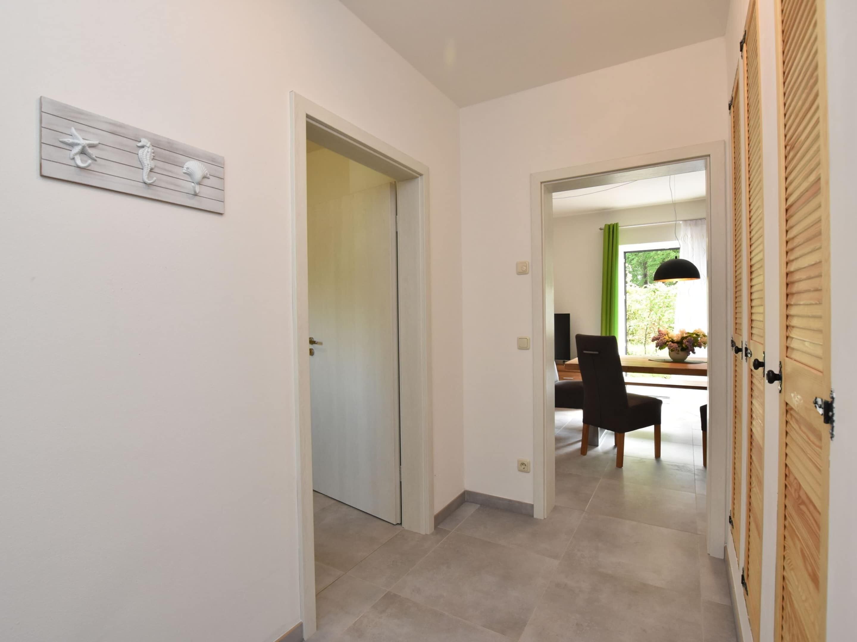 Un pasillo con una puerta de madera, un comedor con mesa y sillas, y vistas al exterior a través de una ventana.