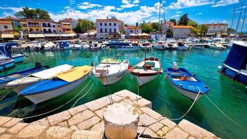 Uma marina com vários barcos atracados, um muro de pedra em primeiro plano e edifícios ao fundo.