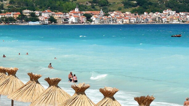 A beach with straw umbrellas and people swimming. - Cozy Apartment in Malinska near Sea (Malinska-Dubasnica)