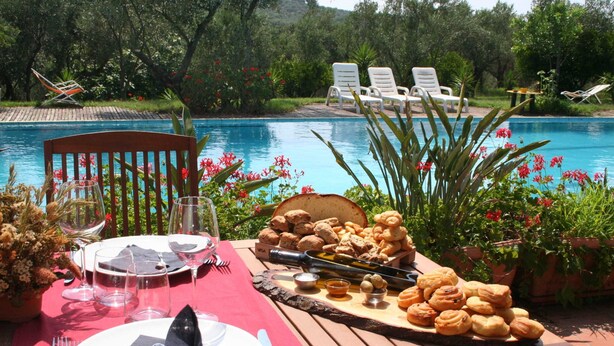 An outdoor dining setup by a pool with a table set for two, including plates, cutlery, glasses, and a bread basket. - Charming Villa in Maida With Pool & Garden (San Pietro a Maida)