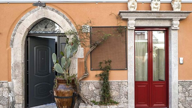 Un bâtiment avec une porte noire, une porte rouge et un grand vase rempli de plantes.