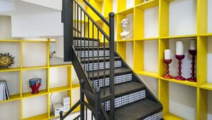 Un escalier avec des rampes noires menant à une étagère jaune et blanche ornée d’objets décoratifs.