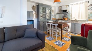 Un salon moderne avec un canapé gris, une table à manger avec des chaises et un coin cuisine doté d’un appareil électroménager rouge.