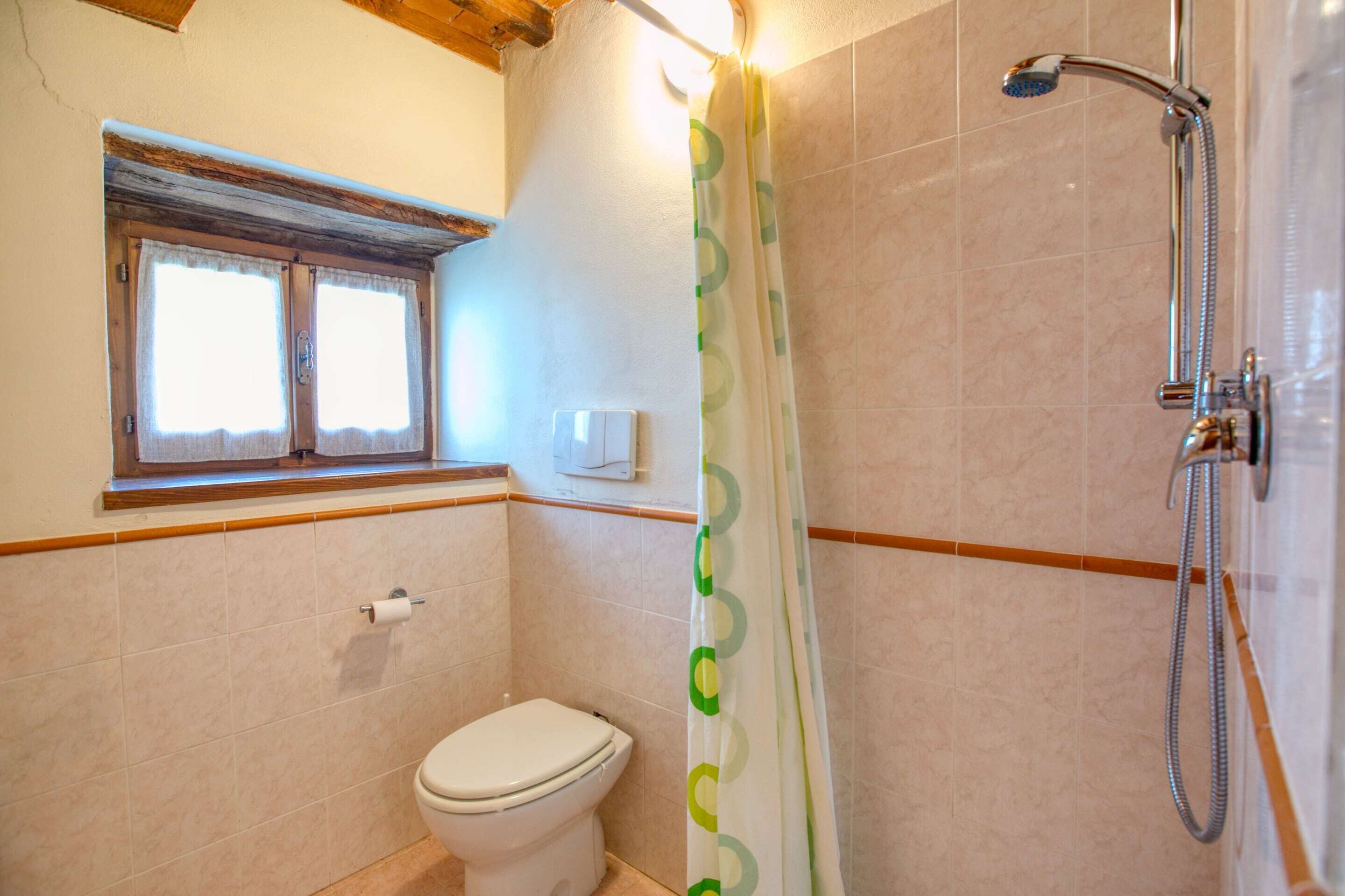 A bathroom with a toilet, a shower with a curtain, and a window above the toilet.