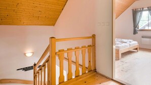 A bedroom with a wooden ceiling, a bed, a window with curtains, and a staircase with a wooden railing. - Holiday Home With a Convenient Location in the Giant Mountains for Summer & Winter (Rudník)