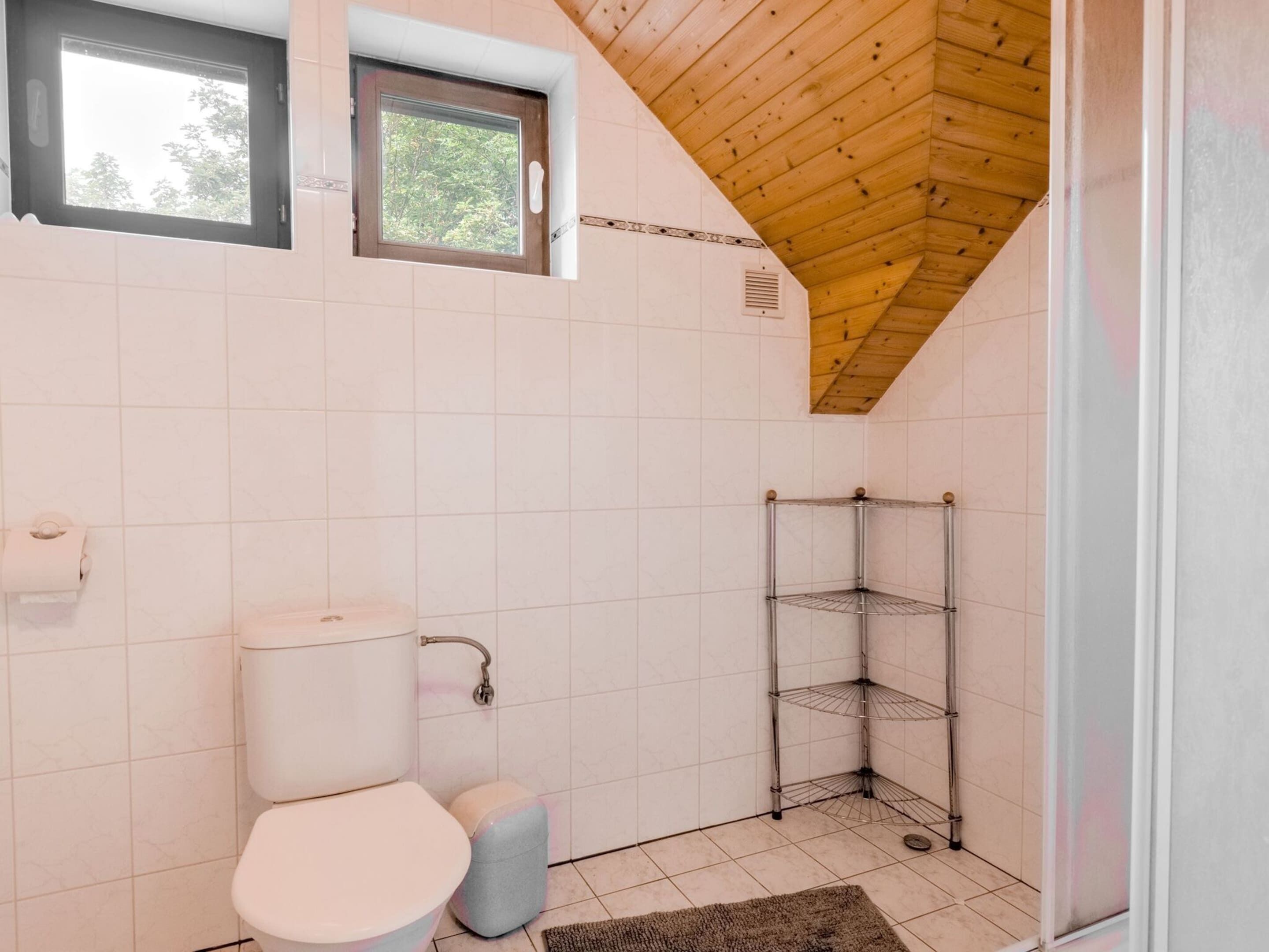 Un bany amb vàter, un petit lavabo, una finestra i un moble prestatge cantonera.