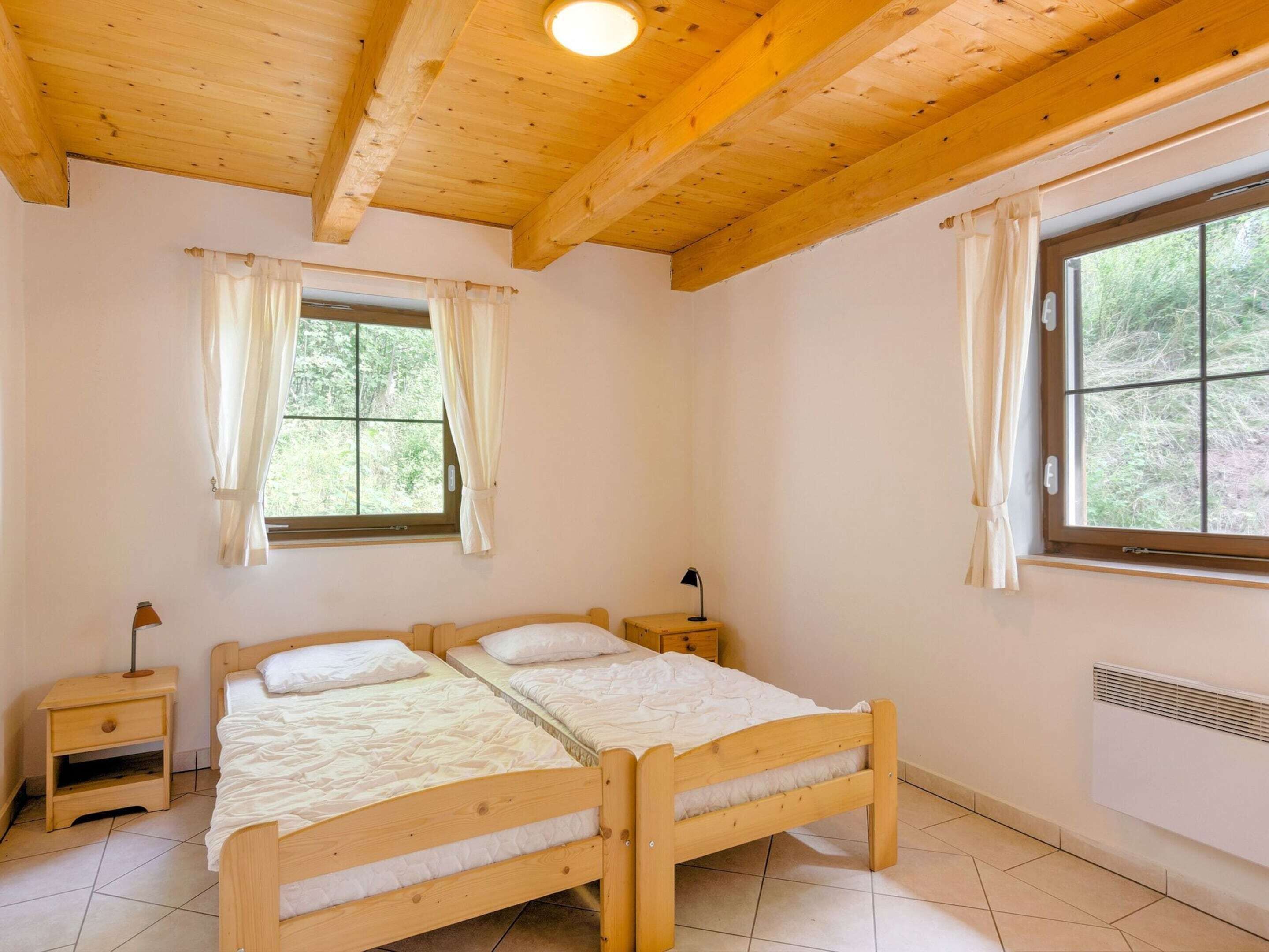 Une chambre avec un lit en bois, deux tables de chevet, une fenêtre avec des rideaux et un radiateur.