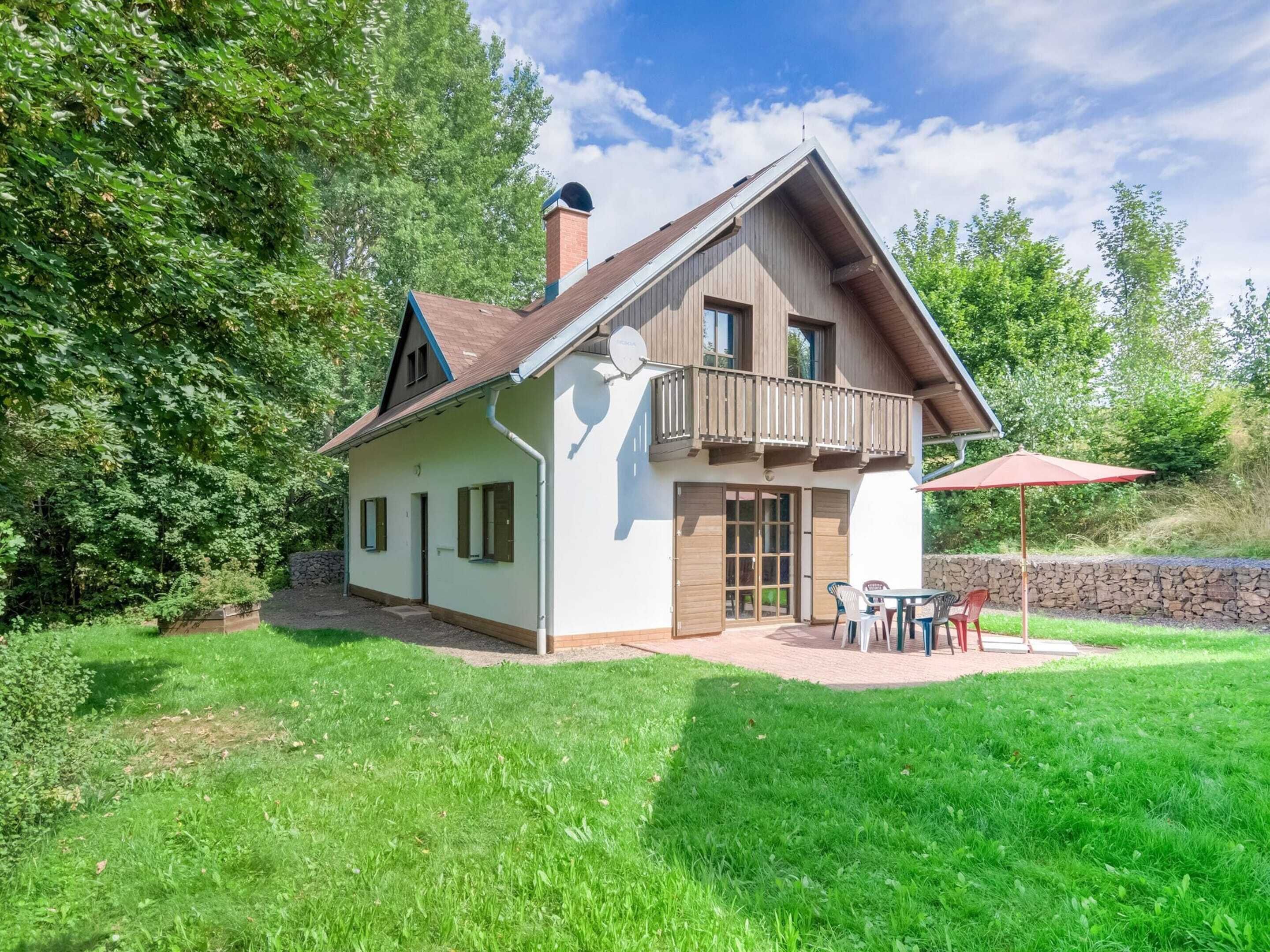 Une maison à deux étages dotée d’un balcon, d’un mur en pierre et d’une terrasse aménagée avec du mobilier d’extérieur.