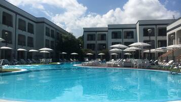 A swimming pool with lounge chairs and umbrellas, surrounded by multi-story buildings with balconies.