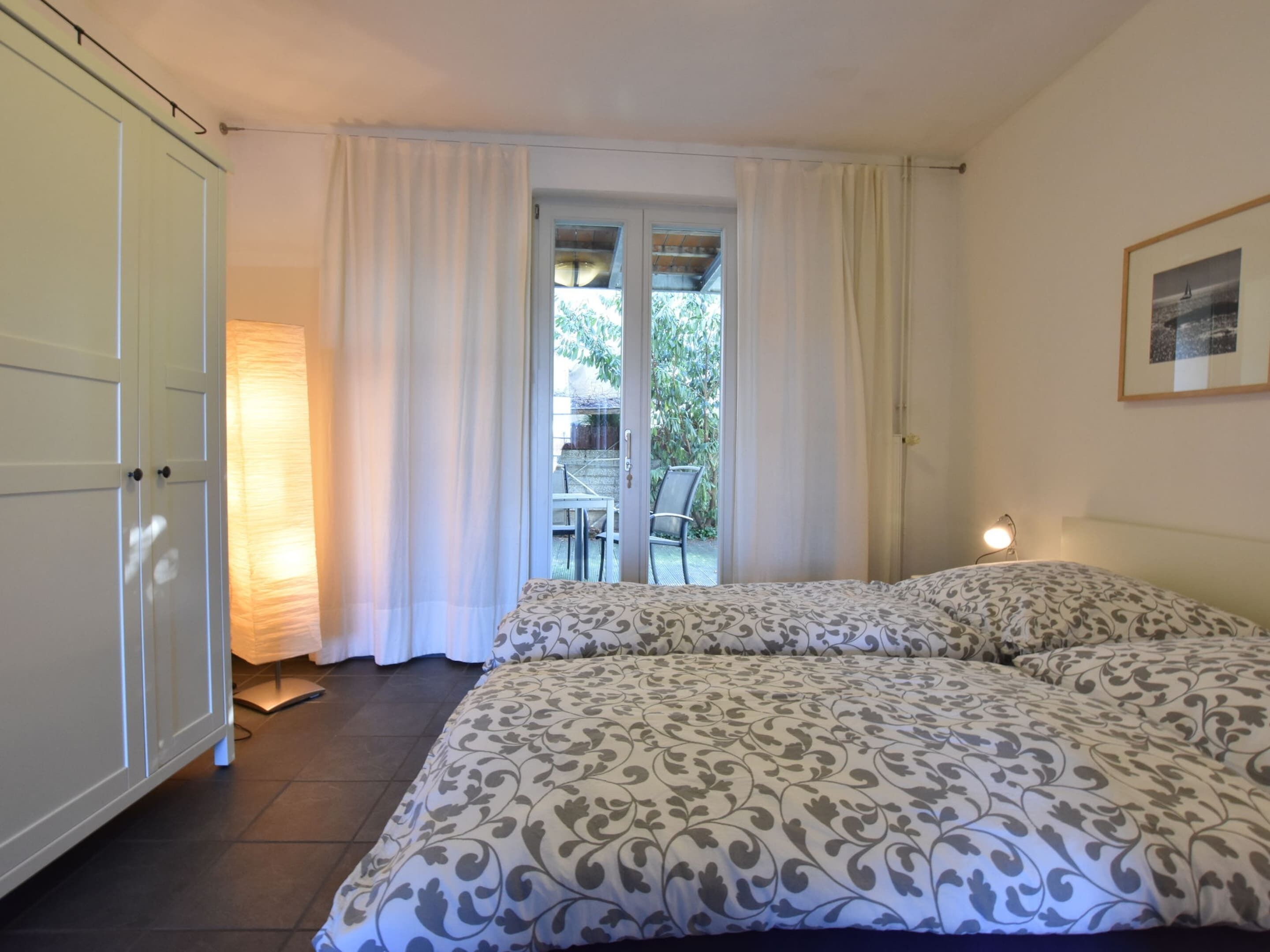 Quarto com duas camas, porta de vidro deslizante para uma varanda e um quadro pendurado na parede.