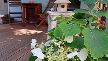 Um deck de madeira com cadeiras, uma mesa, um comedouro de pássaros e folhagem verde.