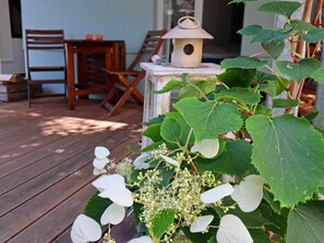 A wooden deck with chairs and a table, a birdhouse, and green foliage. - Wohnung in Wismar mit Garten (Wismar)
