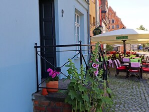 An outdoor café with tables and chairs, a flower pot with pink flowers, and a building with a sign reading "PIER 10". - Wohnung in Wismar mit Garten (Wismar)