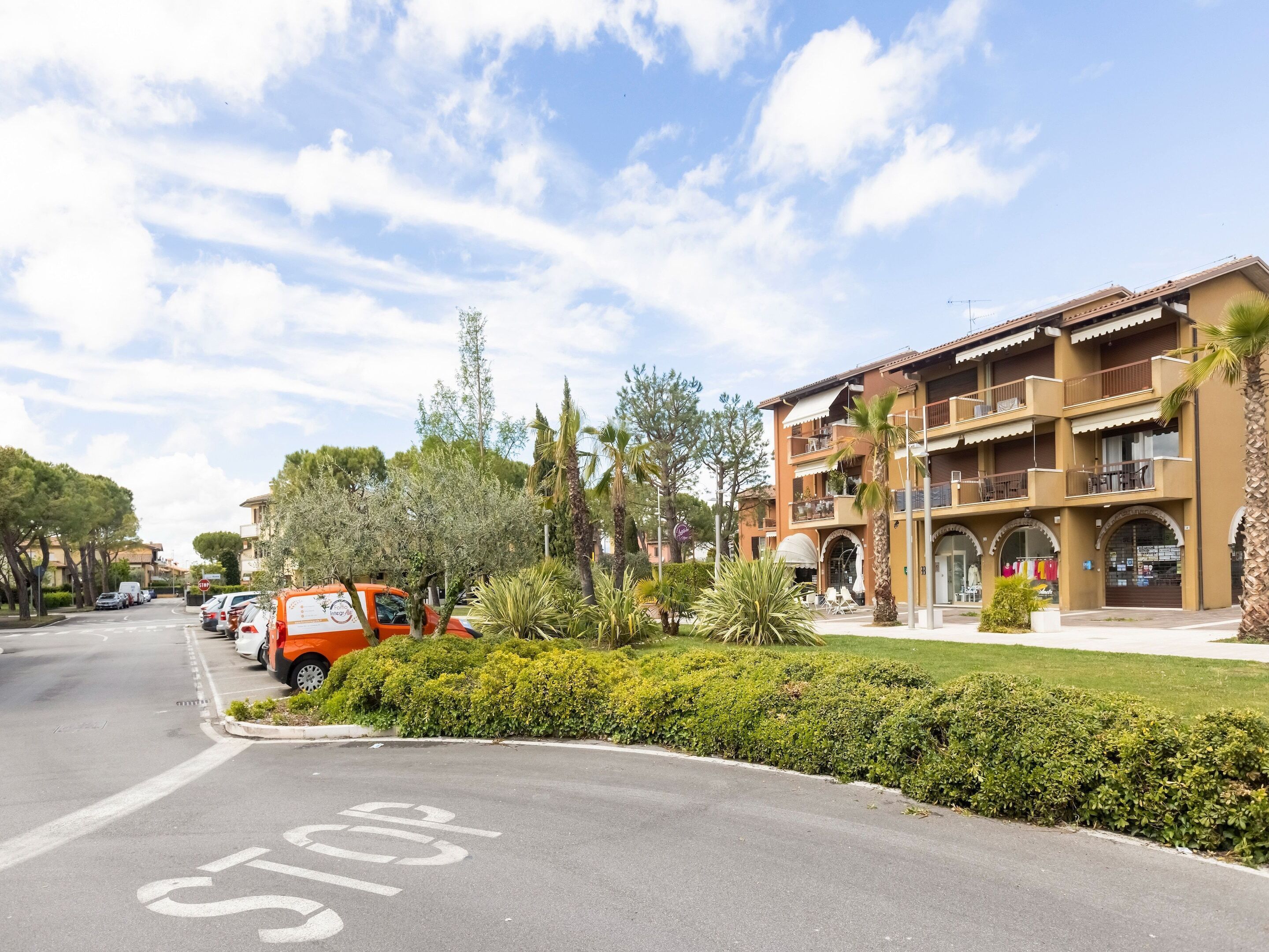 Un hotel a più piani con balconi, un'area parcheggio e un segnale di stop sulla strada.