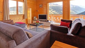 A wooden cabin with a living area featuring a sofa, a TV, and a balcony with mountain views. - Chalet in Les Collons Near Ski Lift (Vex)