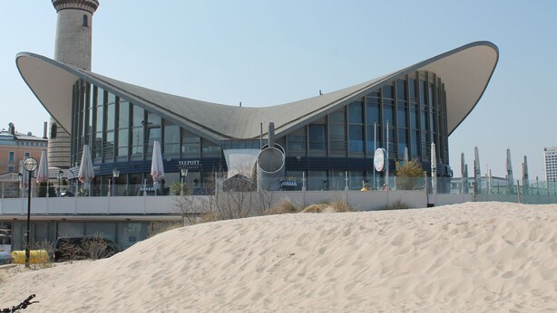 A modern building with a unique curved roof design, a prominent tower, and a sandy foreground. - Modern Holiday Home in Steffenshagen With Terrace (Steffenshagen)