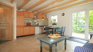 A kitchen with wooden cabinets, a dining table with chairs, and a view of the outdoors through a glass door. - Modern Holiday Home in Steffenshagen With Terrace (Steffenshagen)