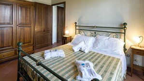 A neatly made bed with white linens and towels, a wooden wardrobe, and a small bedside table with a lamp. - Belvilla by OYO Villa Santa Caterina (Cortona)
