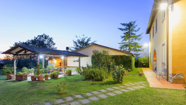 A well-maintained garden with a patio area, a covered seating space, and a pathway leading to a building. - Belvilla by OYO Villa Santa Caterina (Cortona)