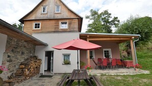 A two-story wooden house with a stone wall and a wooden deck. - Bedroom Farmhouse by the Woods (Malecov)