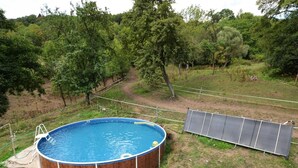 A round swimming pool with a wooden deck, surrounded by a grassy area and trees. - Bedroom Farmhouse by the Woods (Malecov)