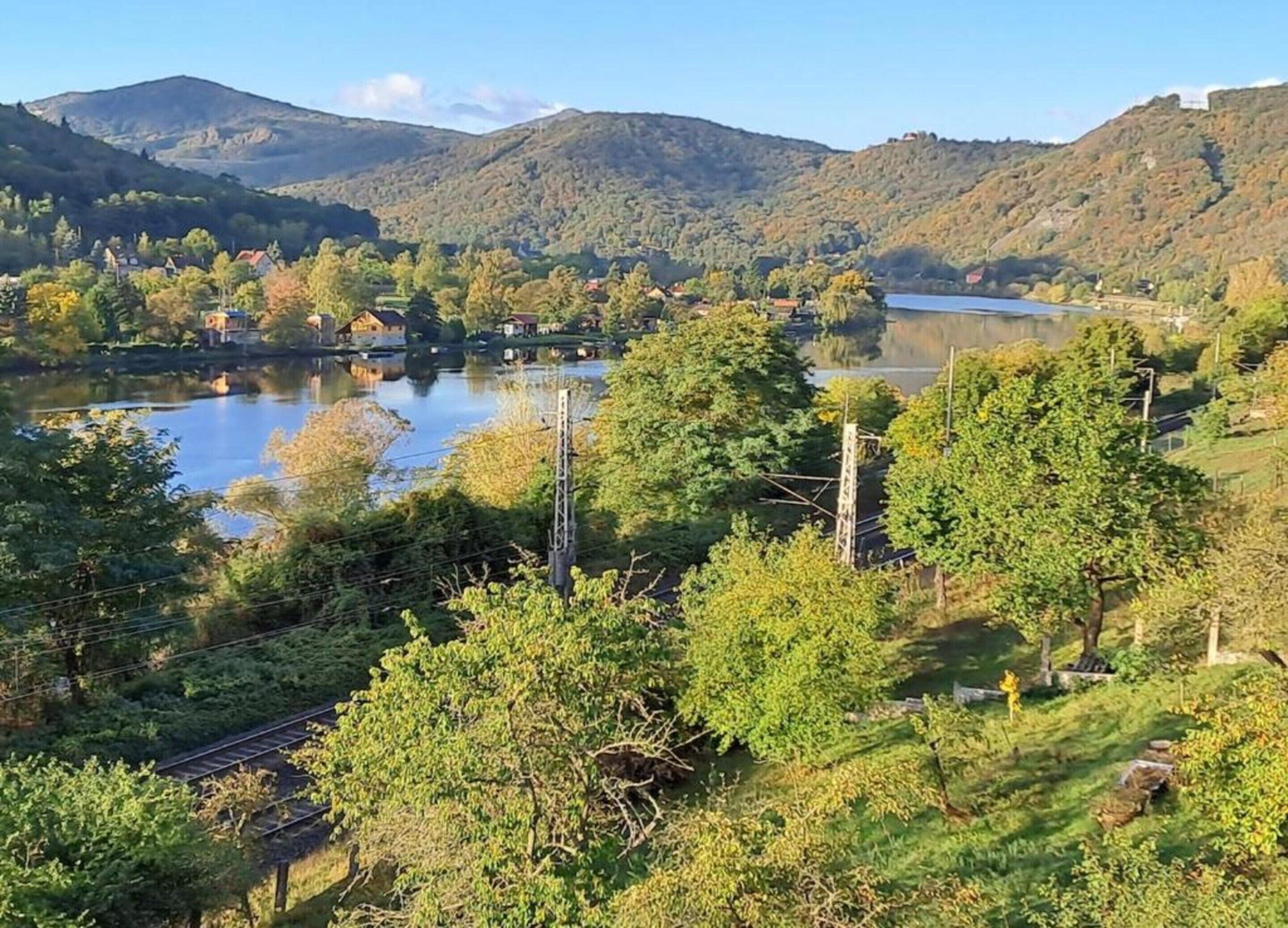 Une vue pittoresque d’un lac entouré de collines, avec une voie ferrée au premier plan.