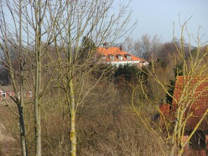 A house with a red roof, surrounded by leafless trees and a hill in the background. - Idyllische Wohnung an der Ostseekueste (Damshagen)