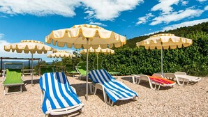 Una spiaggia con numerosi lettini e ombrelloni, circondata da vegetazione e colline.