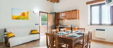 A cozy living area with a sofa, wooden dining table, and chairs, a kitchen with wooden cabinets, and a large window.