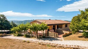 Una casa a un piano con tetto in tegole, circondata da un vialetto sterrato e un recinto in legno.
