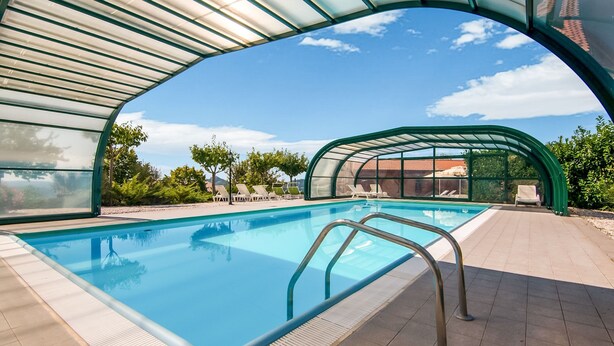 Piscina trasparente con struttura in vetro, circondata da sdraio e solarium piastrellato.