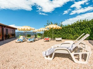 A beach area with multiple sun loungers and umbrellas, a building with a tiled roof, and a hedge in the background. - Farmhouse in Apecchio With Pool (Apecchio)